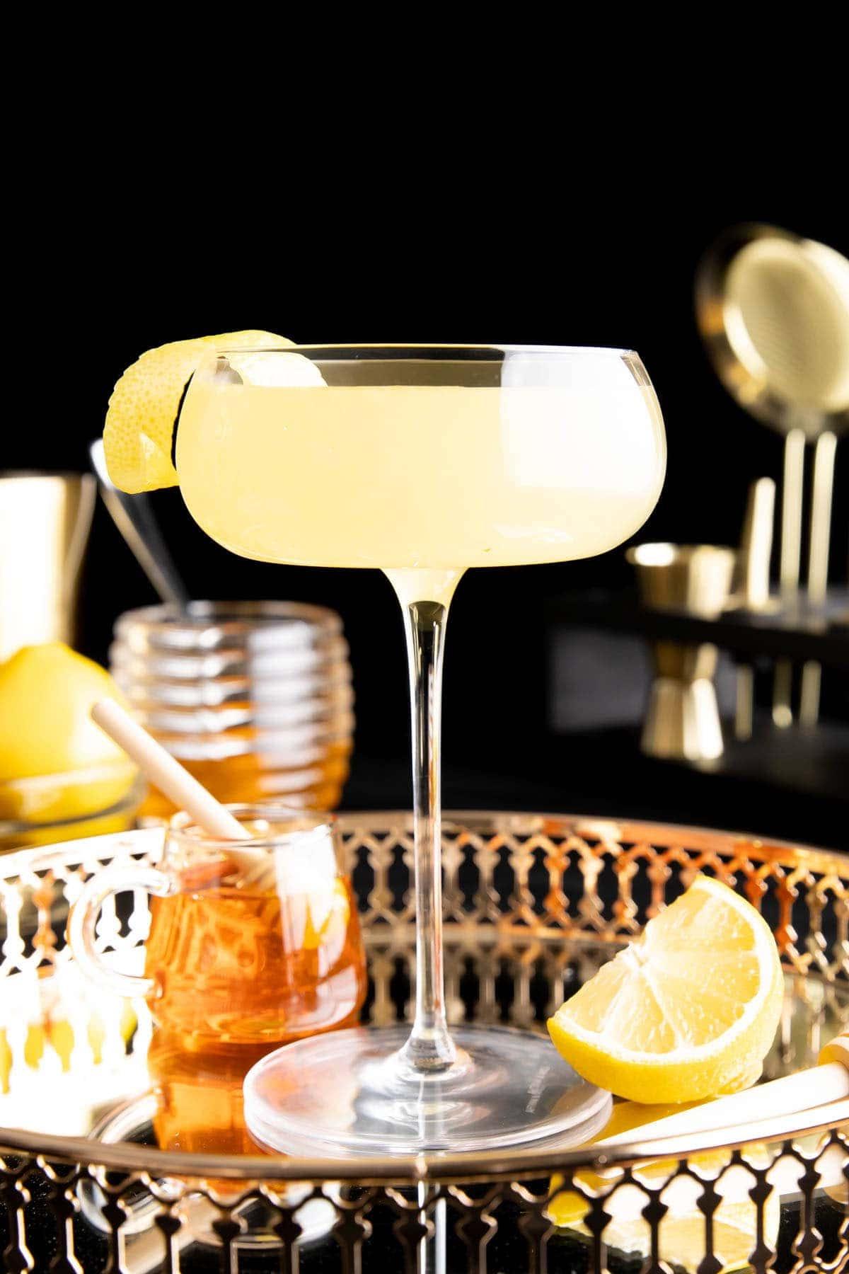Ein Bee’s Knees Cocktail in einem Glas mit Zitronengarnitur