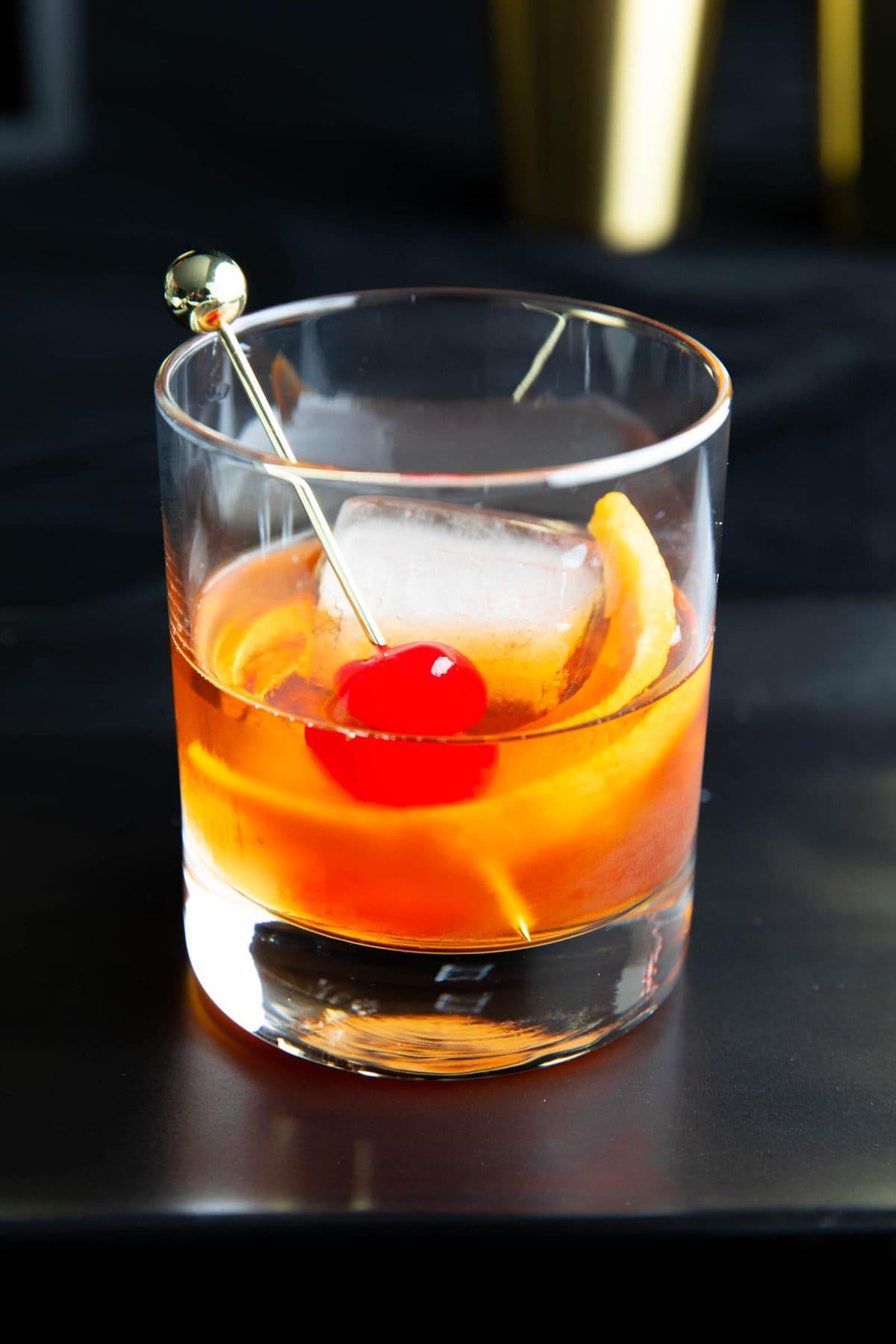 Ein Old Fashioned Whiskey-Cocktail, garniert mit Orangenzeste und einer Maraschino-Kirsche, nahaufnahme