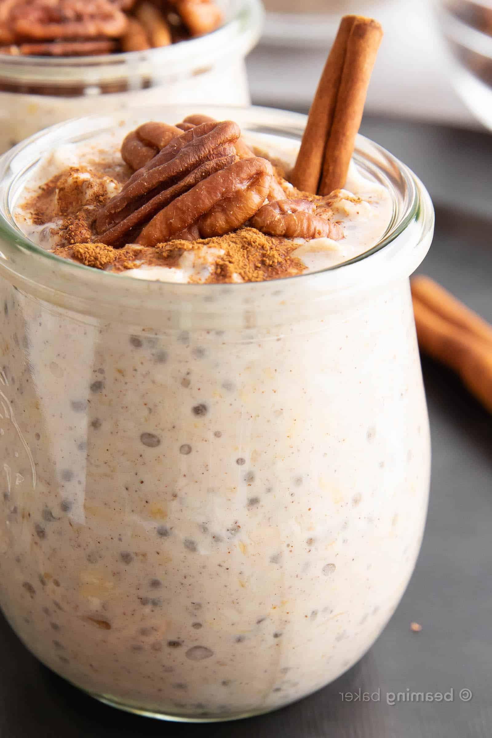Super Nahaufnahme eines Glases Ahorn-Pekannuss Overnight Oats, garniert mit Zimtstange und Pekannüssen