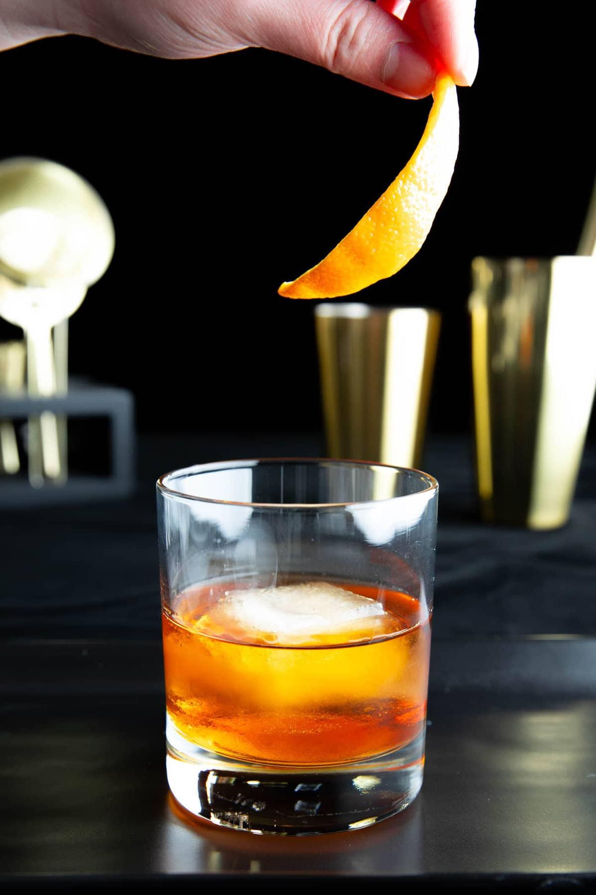 Eine Hand, die eine Orangenschale als Garnitur zu einem Old Fashioned Cocktail hinzufügt