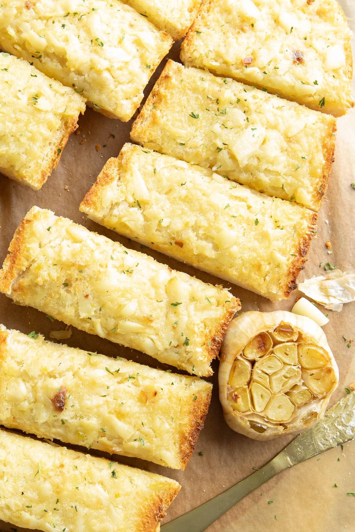 Knoblauchbrotscheiben auf einem Serviertablett mit einem Kopf geröstetem Knoblauch und einem Streichmesser