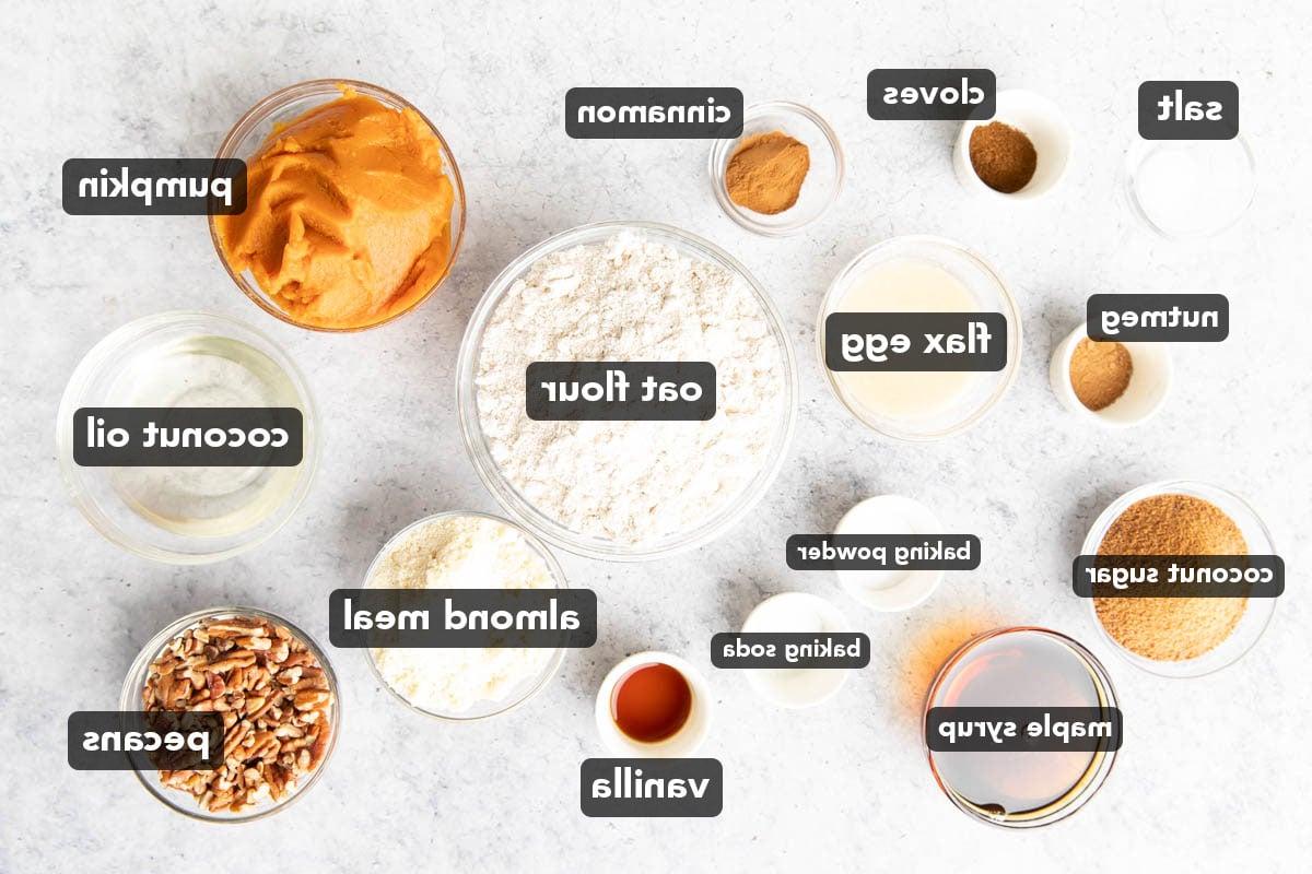 Vegane Glutenfreie Kürbis-Streuselkuchen-Zutaten, vorgemessen in Glasschalen, darunter Kürbispüree, Kokosblütenzucker, Mehl, Leinsamen-Eier, Kokosöl und mehr.