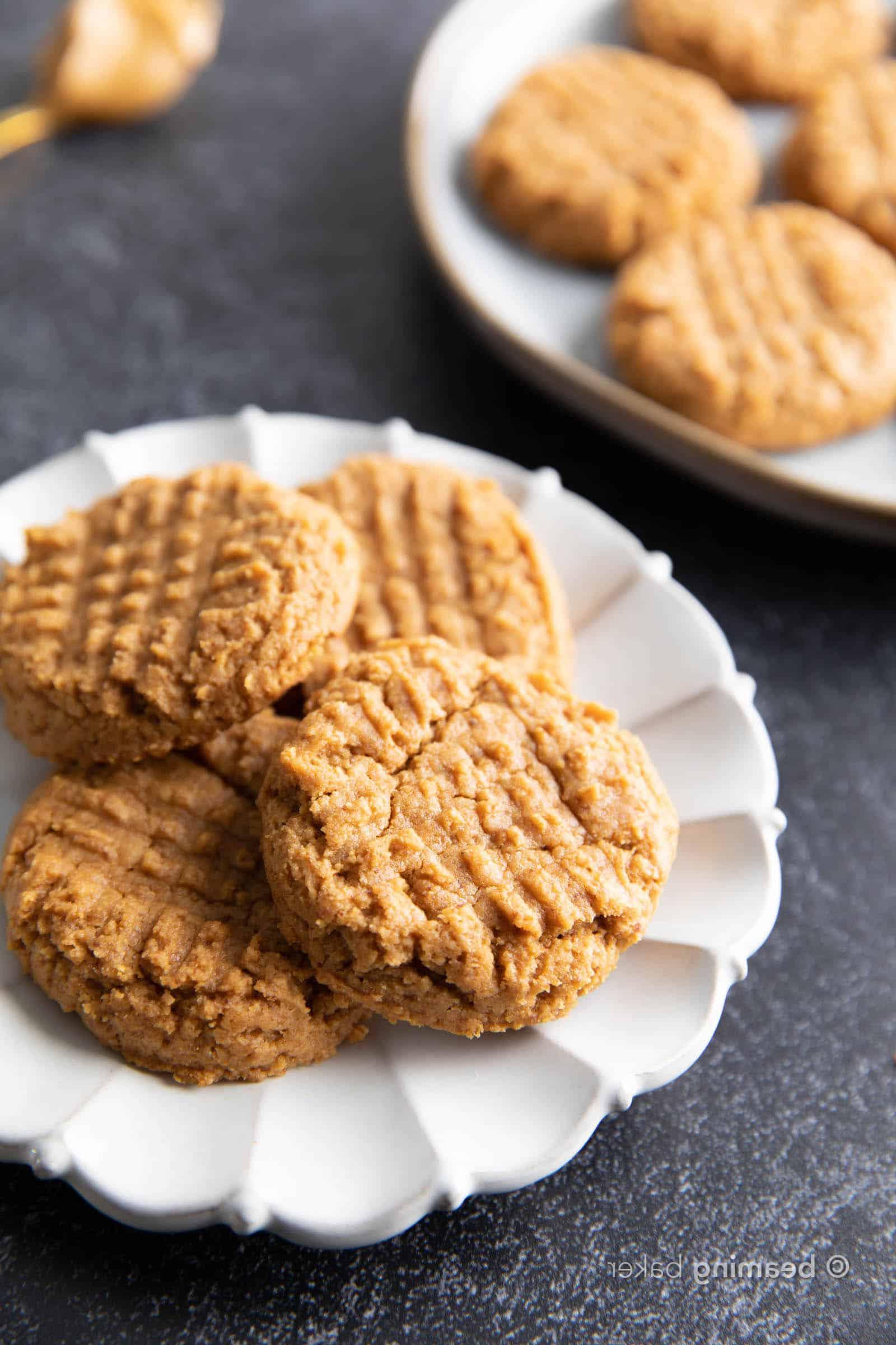 Vier glutenfreie Erdnussbutter-Kekse gestapelt und auf einem weißen Teller verteilt.