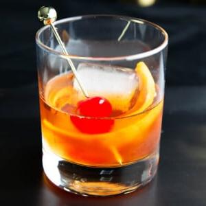 Ein Old Fashioned Cocktail Rezept, serviert in einem Glas mit Kirsch- und Orangenscheiben-Garnitur