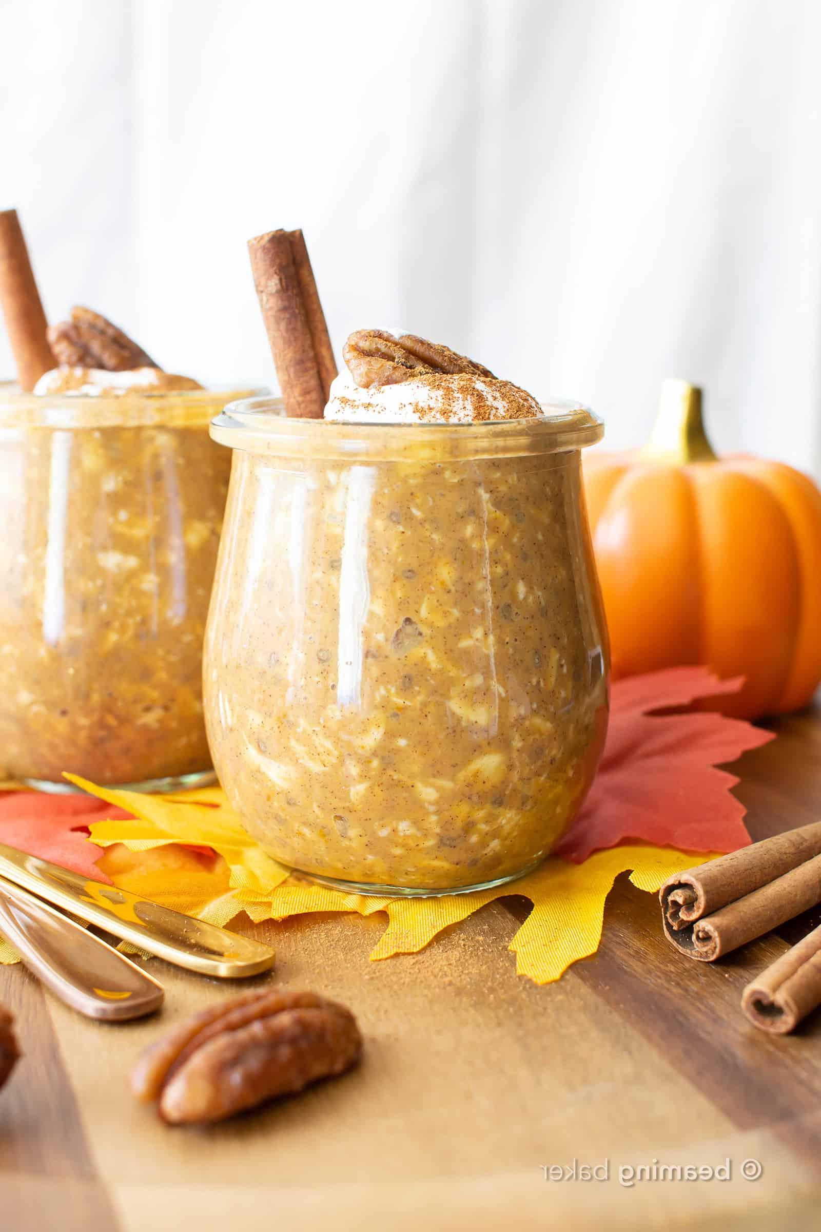 Kürbis-Overnight-Oats 2 Zwei Gläser gefüllt mit Kürbis Overnight Oats, serviert mit Pekannüssen und Zimtstangen