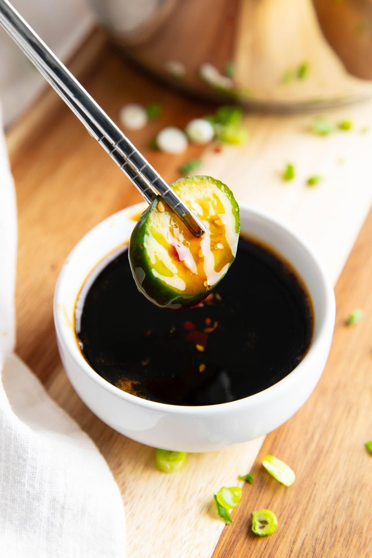 Jemand dippt eine Gurkenscheibe in Unagi-Soße.